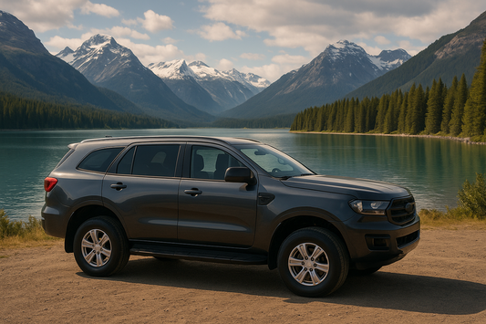 Dark gray SUV parked beside a calm alpine lake with snow-capped mountains and evergreen forest in the background — ideal for banner use highlighting roof rack compatibility in New Zealand.