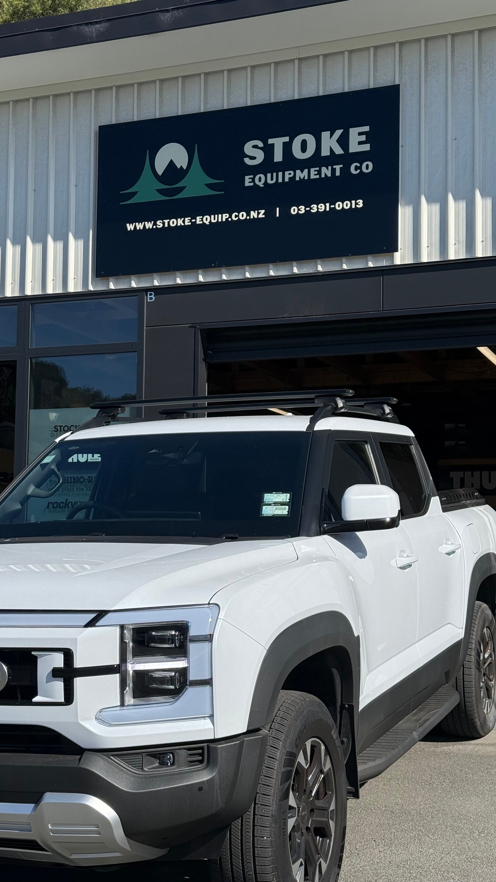 White BYD Shark 6 parked in front of Stoke Equipment Co building after being fitted with Thule WingBar Evo Roof Racks