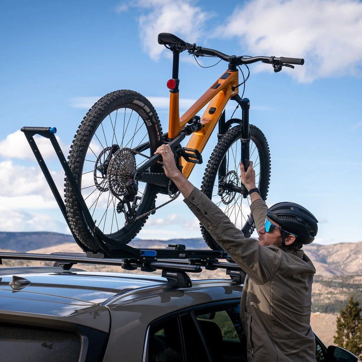 Person securing a bicycle on a car roof rack with a scenic background