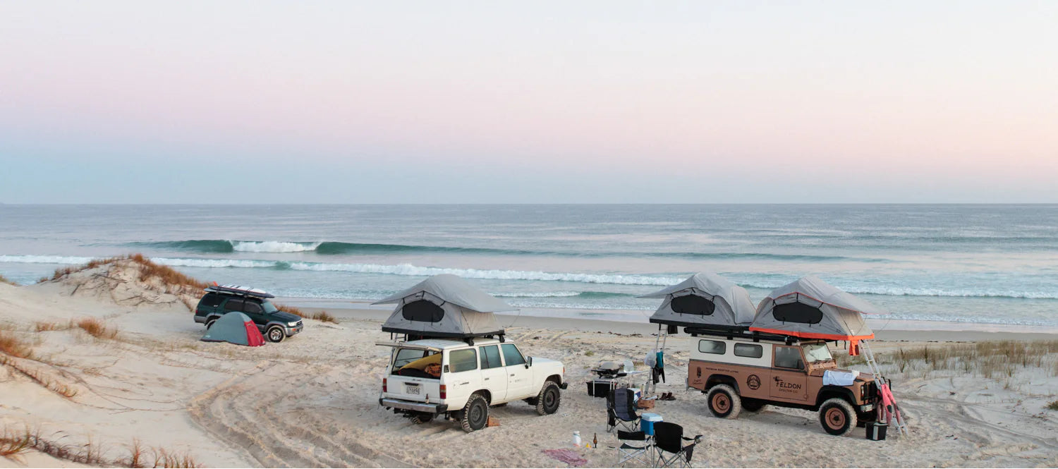 Three vehicles with rooftop tents on a sandy beach with ocean in the background