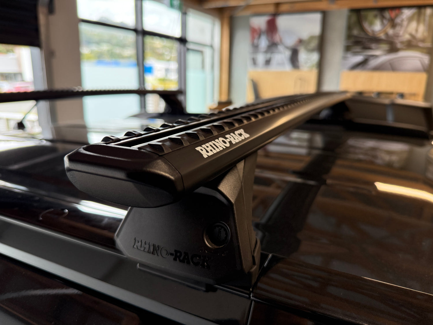 Close-up of a Rhino-Rack roof rack system on a vehicle, with blurred indoor background.