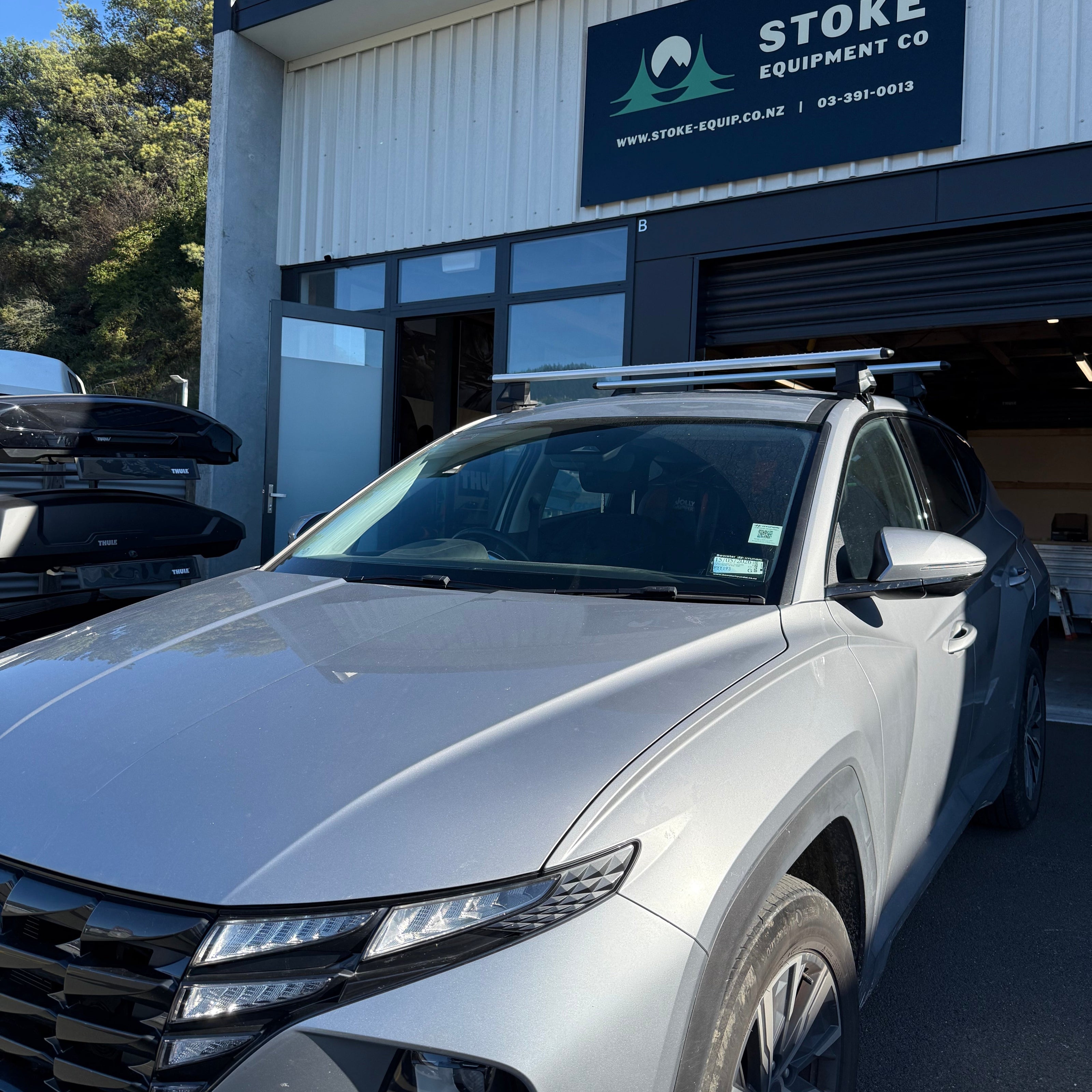 hyundai tucson fitted with silver thule wingbar evo roof racks, parked in front of stoke equipment co nelson roof rack store