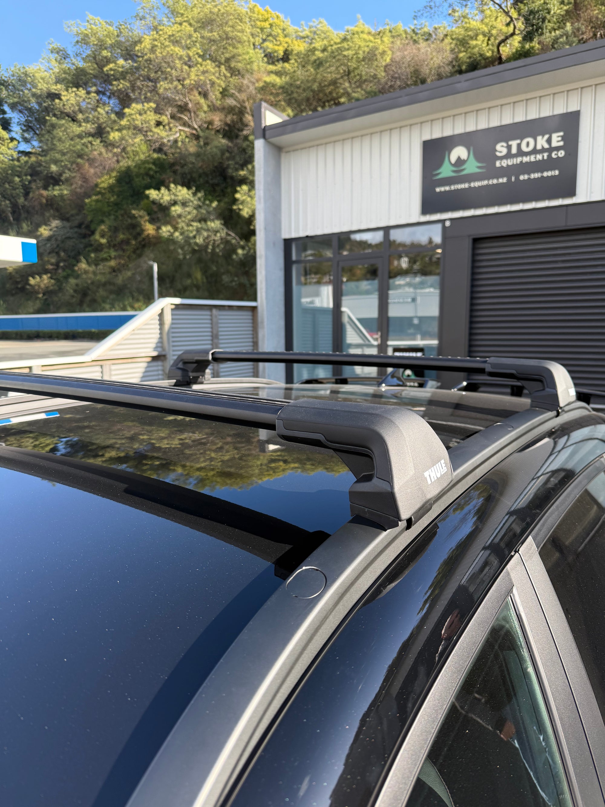 Thule 720600 Flush Rail Roof Rack System mounted to a vehicle in front of a building with 'Stoke Equipment Co - Eoof Rack Store Nelson' branding