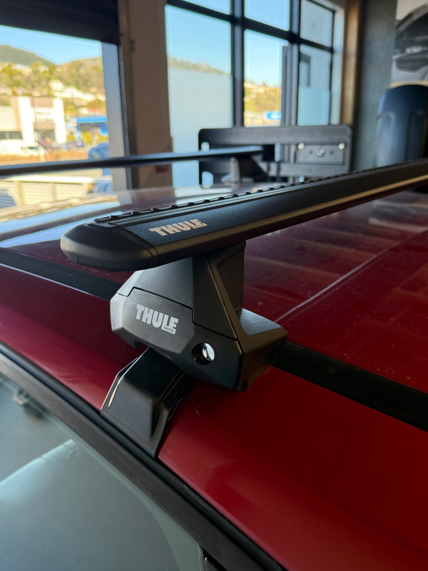 Close-up of a red car door with a Thule Wingbar Evo 710500 clamp mount system attached, at Stoke equipment co nelson's thule specialist store