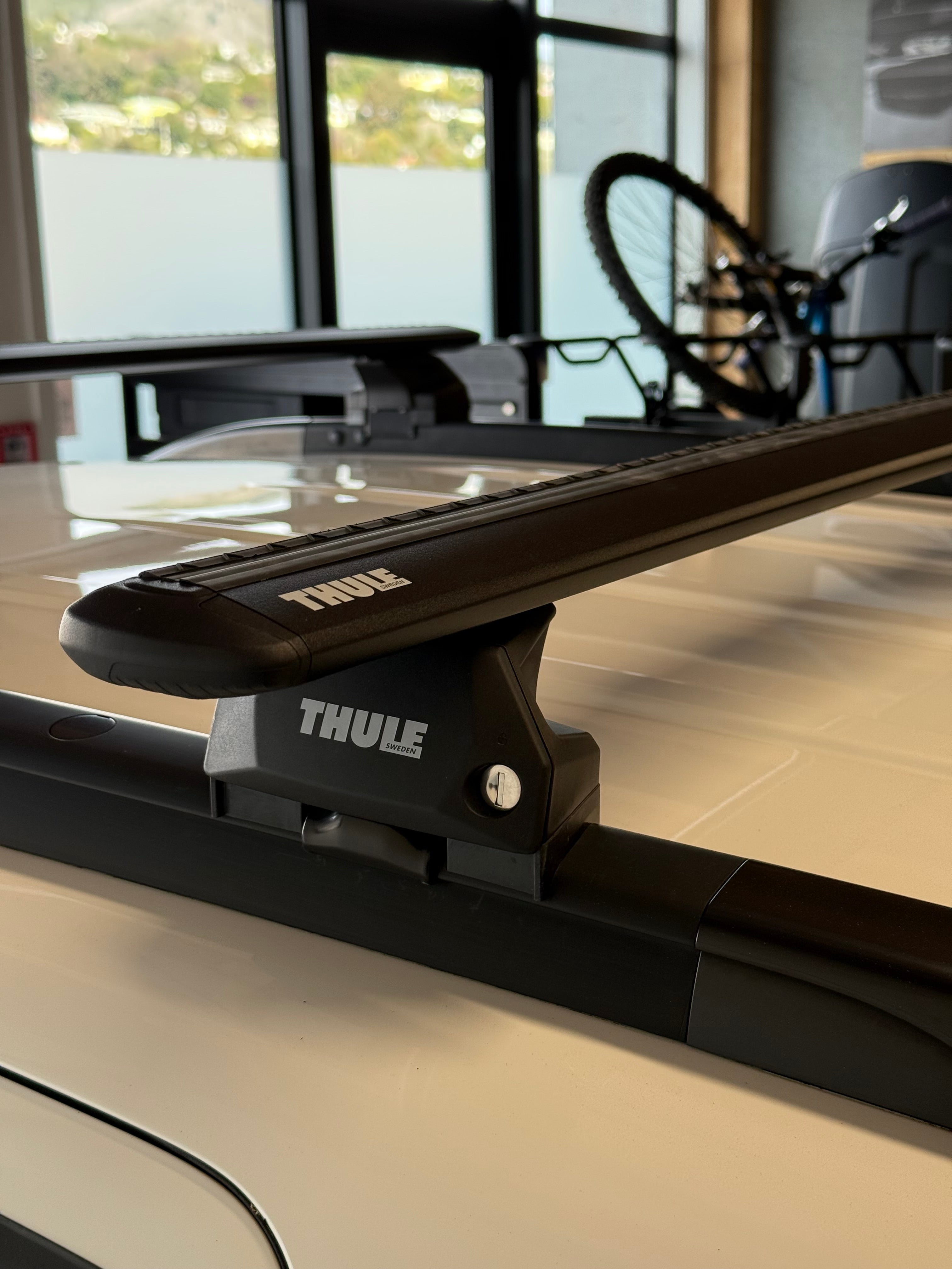 Close-up of a Thule 710600 flush rail roof rack attached to a vehicle, with a bicycle rack in the backgound