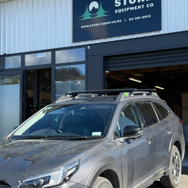 Subaru Outback fitted with Rhino-Rack Roof Racks in front of a building with 'Stoke Equipment Co' sign.