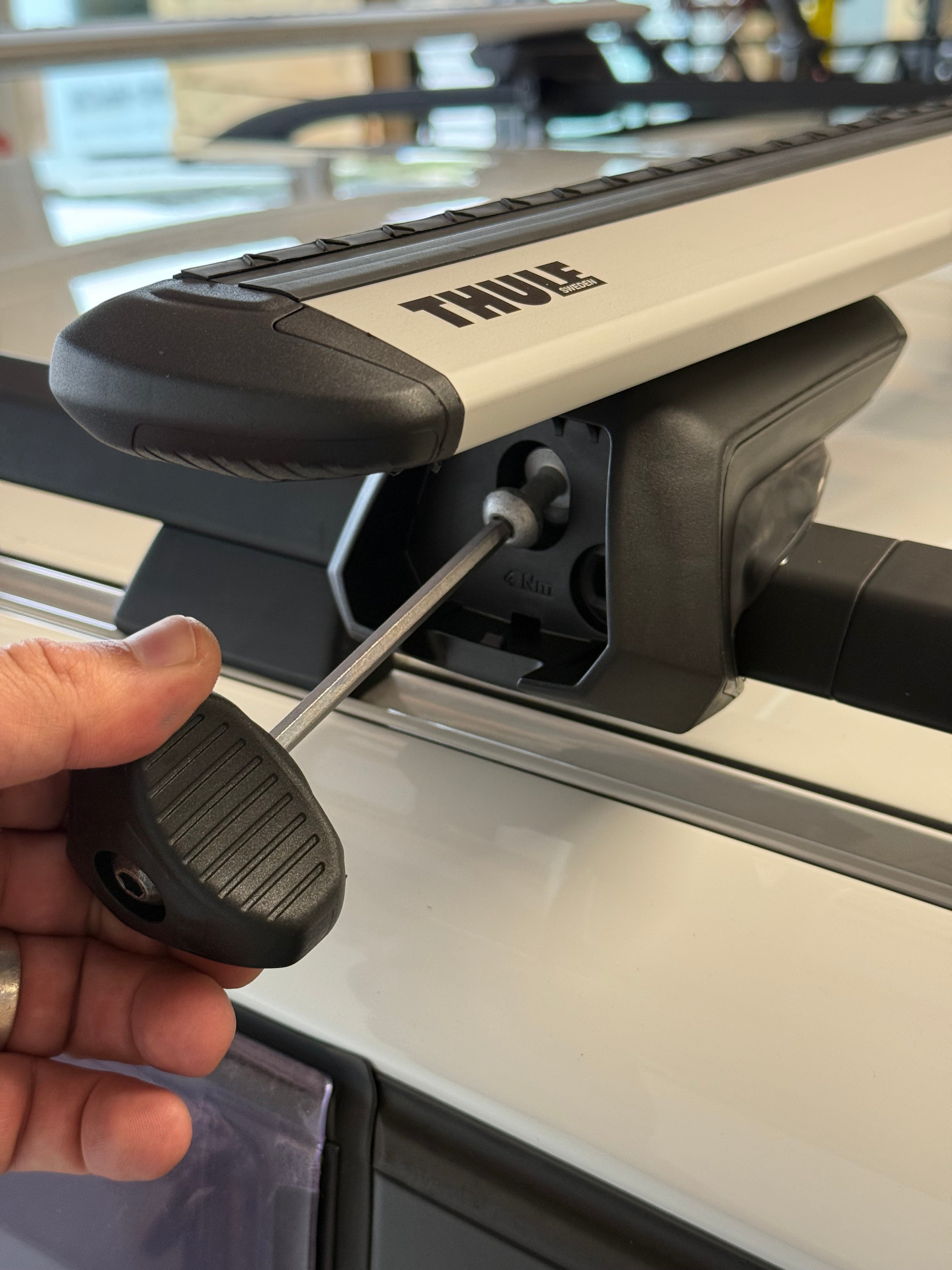Person using a tool to install a thule raised rail roof rack onto a vehicle.
