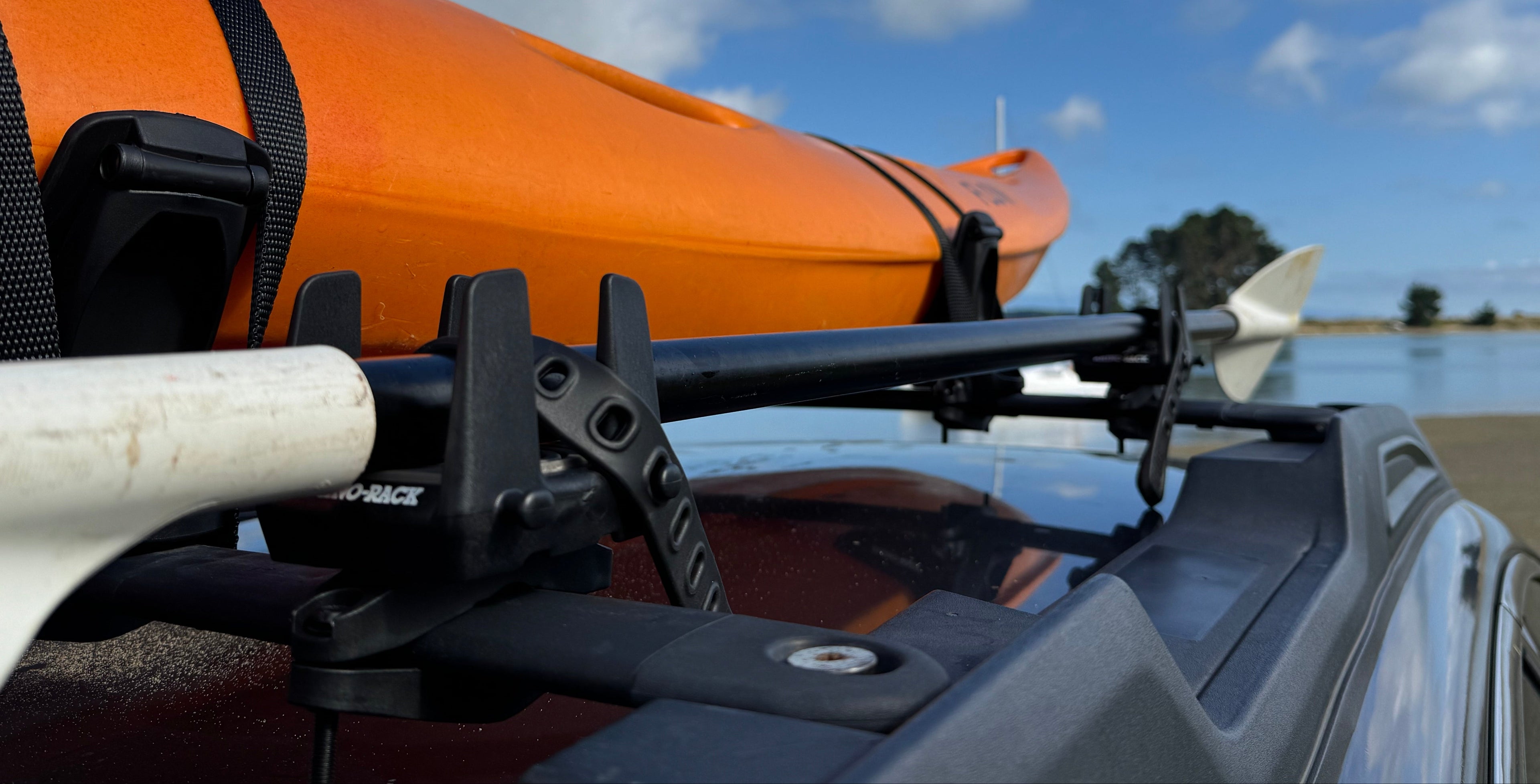 Orange kayak attached to a vehicle with a blue sky and clouds in the background