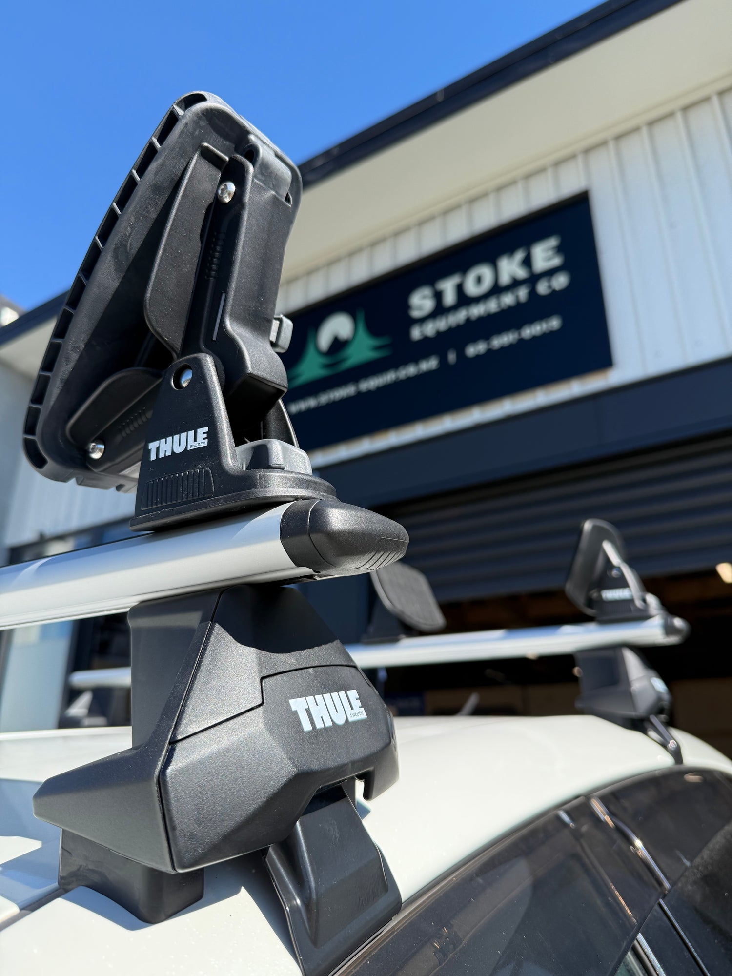Close-up of a Thule kayak rack with Stoke Equipment Co Roof Rack Store building in the background