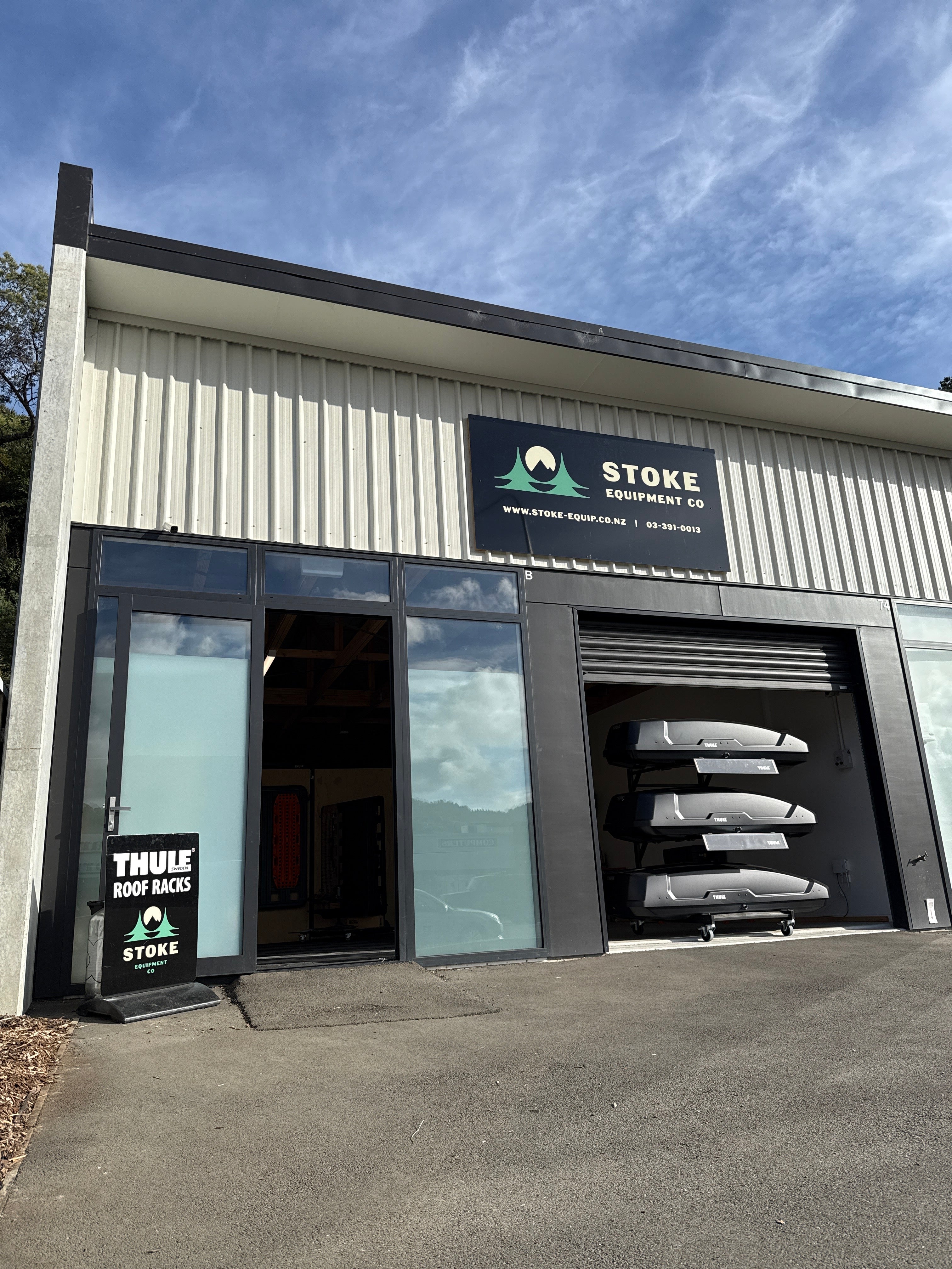 Exterior picture of Stoke Equipment Co Roof Rack Store in Nelson, showing branding outside the building on a clear blue sky day