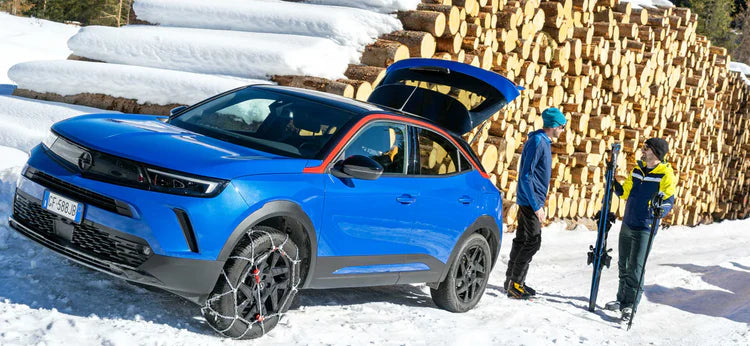 Konig XG Cross snow chains on an opel mokka in a snowy village next to a pile of firewood