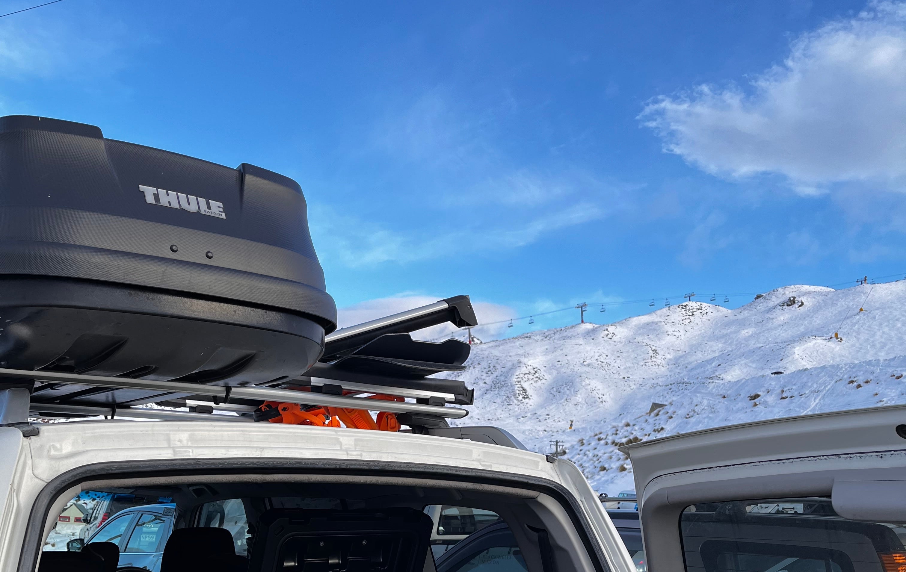 NZ ski road trip with snowboards and skis in s a ski carrier, roof racks and roof box loaded for winter missions parked at the base of coronet peak