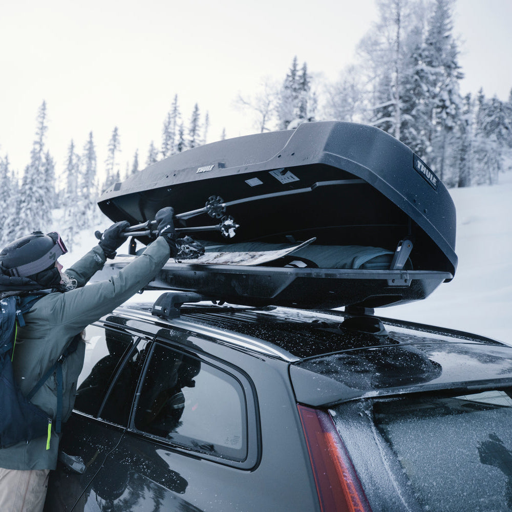 Image of a skier loading skis into a thule force xt roof box, in a ski field carpark