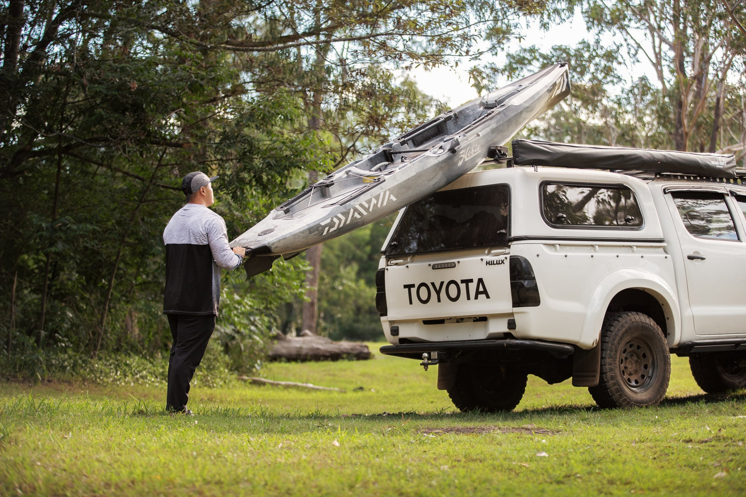 Image of a man, loading a Hobie Fishing Kayak onto his Toyota HIlux fitted with Rhino-Rack Roof Racks and Kayak Carrier