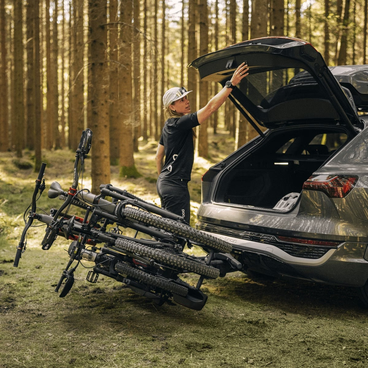 Person loading bicycles onto a car with a bike rack in a forest setting