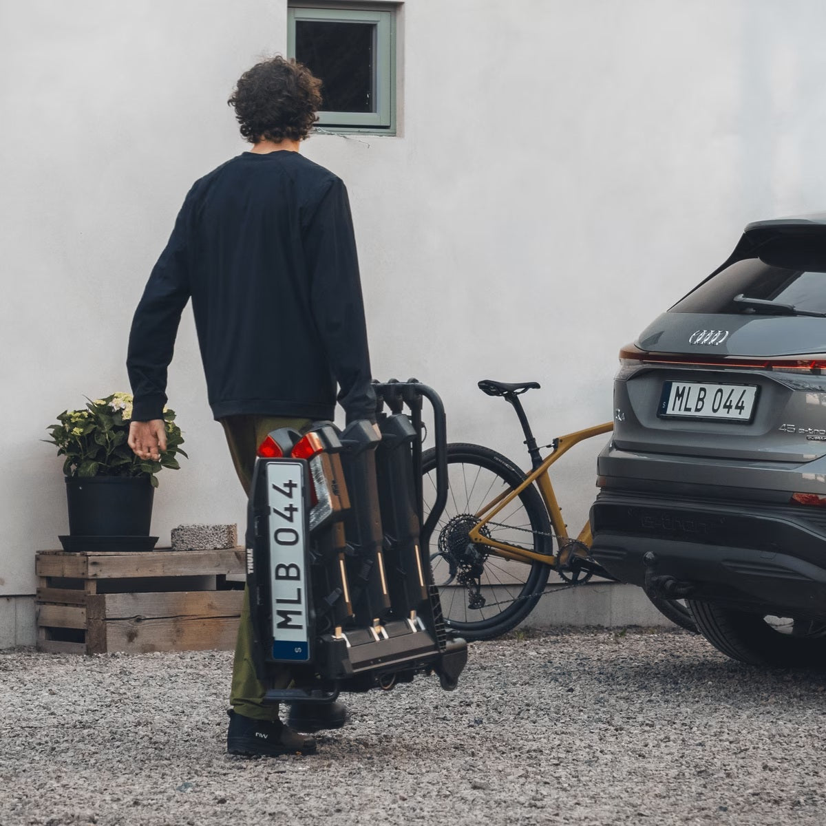 Person using a bike carrier attached to a car, with a bicycle on the ground.