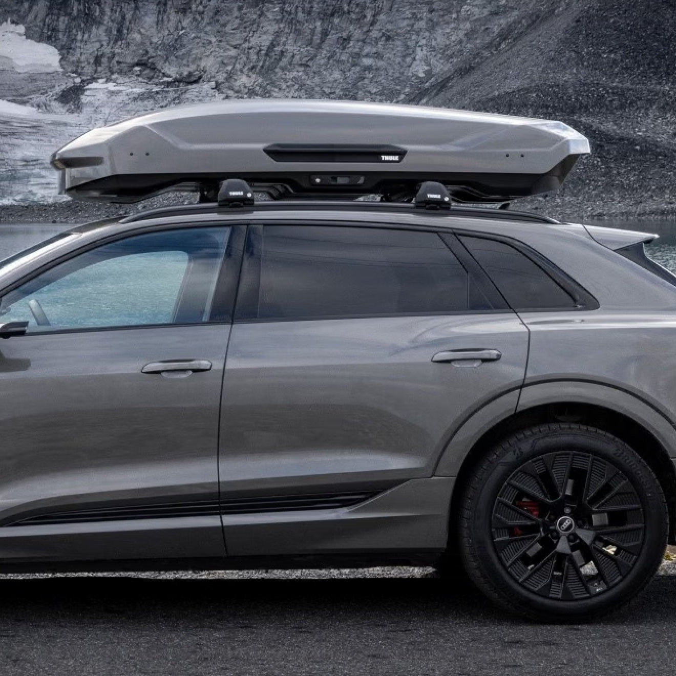 Silver car with a roof box parked near a body of water.