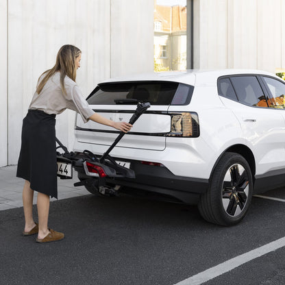 Woman attaching a bike rack to a white car in an urban setting