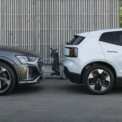 Two cars, one gray and one white, parked side by side on a road with a bike rack attached.